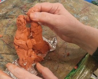 A pair of hands working on a clay sculpture. The clay is terracotta, and the sculpture is around hand size.