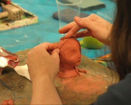 A pair of hands making a small head in terracotta clay