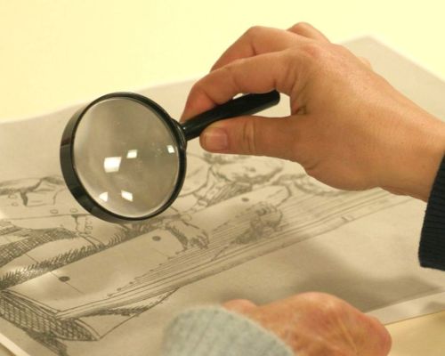 A hand holding a magnifying glass up to a black and white drawing.