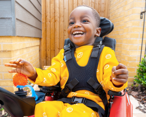 A young child wearing a bright yellow top and a brighter smile is using a mobility aid
